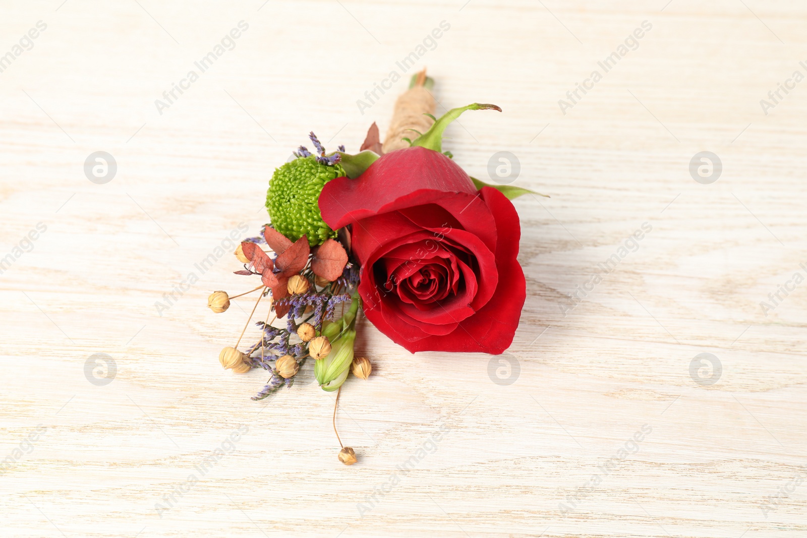 Photo of Stylish boutonniere with red rose on light wooden table, closeup