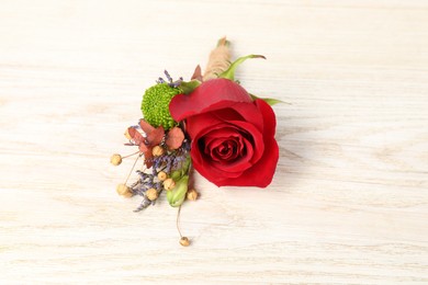 Photo of Stylish boutonniere with red rose on light wooden table, closeup