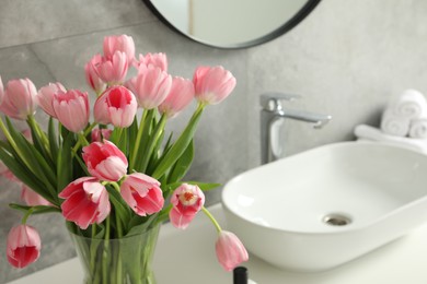 Photo of Vase with beautiful pink tulips near sink in bathroom, closeup