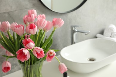 Vase with beautiful pink tulips near sink in bathroom, closeup