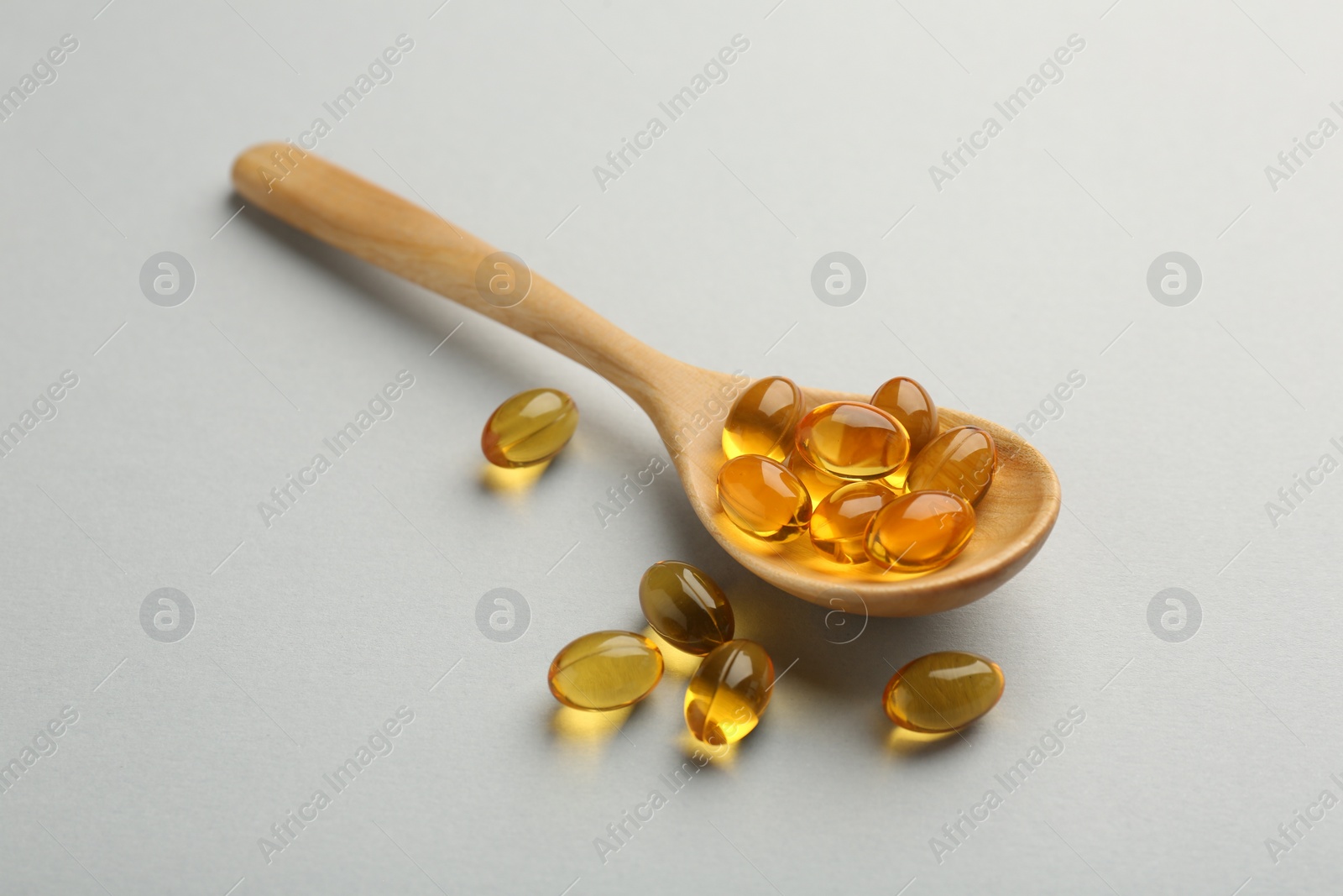 Photo of Vitamin capsules in wooden spoon on light grey background. Health supplement