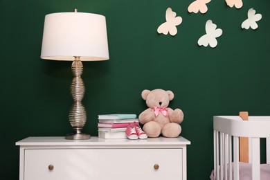Photo of Books, booties, lamp and teddy on chest of drawers in baby room