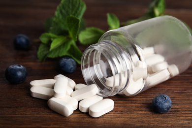 Photo of Bottle with vitamin pills and blueberries on wooden table, closeup