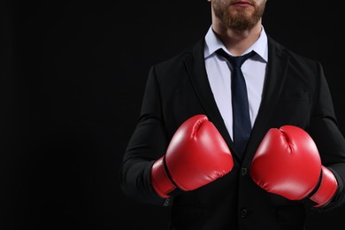 Photo of Businessman in suit wearing boxing gloves on black background, closeup. Space for text