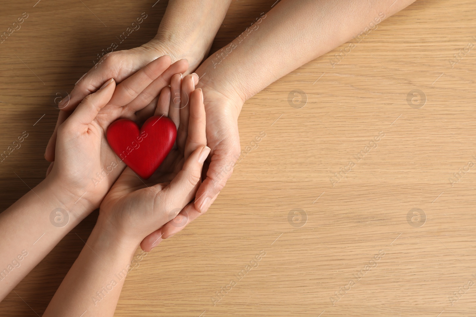 Photo of Young and elderly women holding red heart at wooden table, top view. Space for text