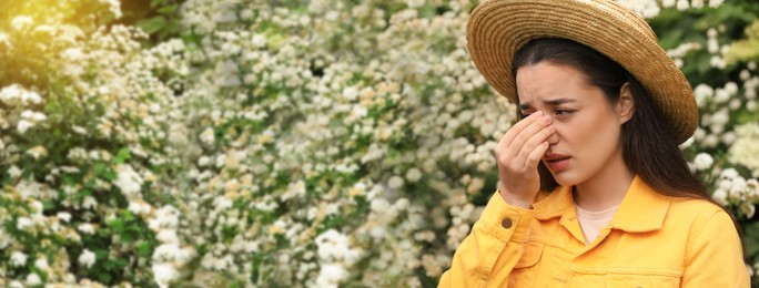 Image of Woman suffering from seasonal pollen allergy near blossoming tree on spring day. Banner design with space for text