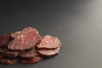 Photo of Pieces of delicious beef jerky on dark table, closeup. Space for text