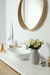 Photo of Vase with beautiful white roses and toiletries near sink in bathroom