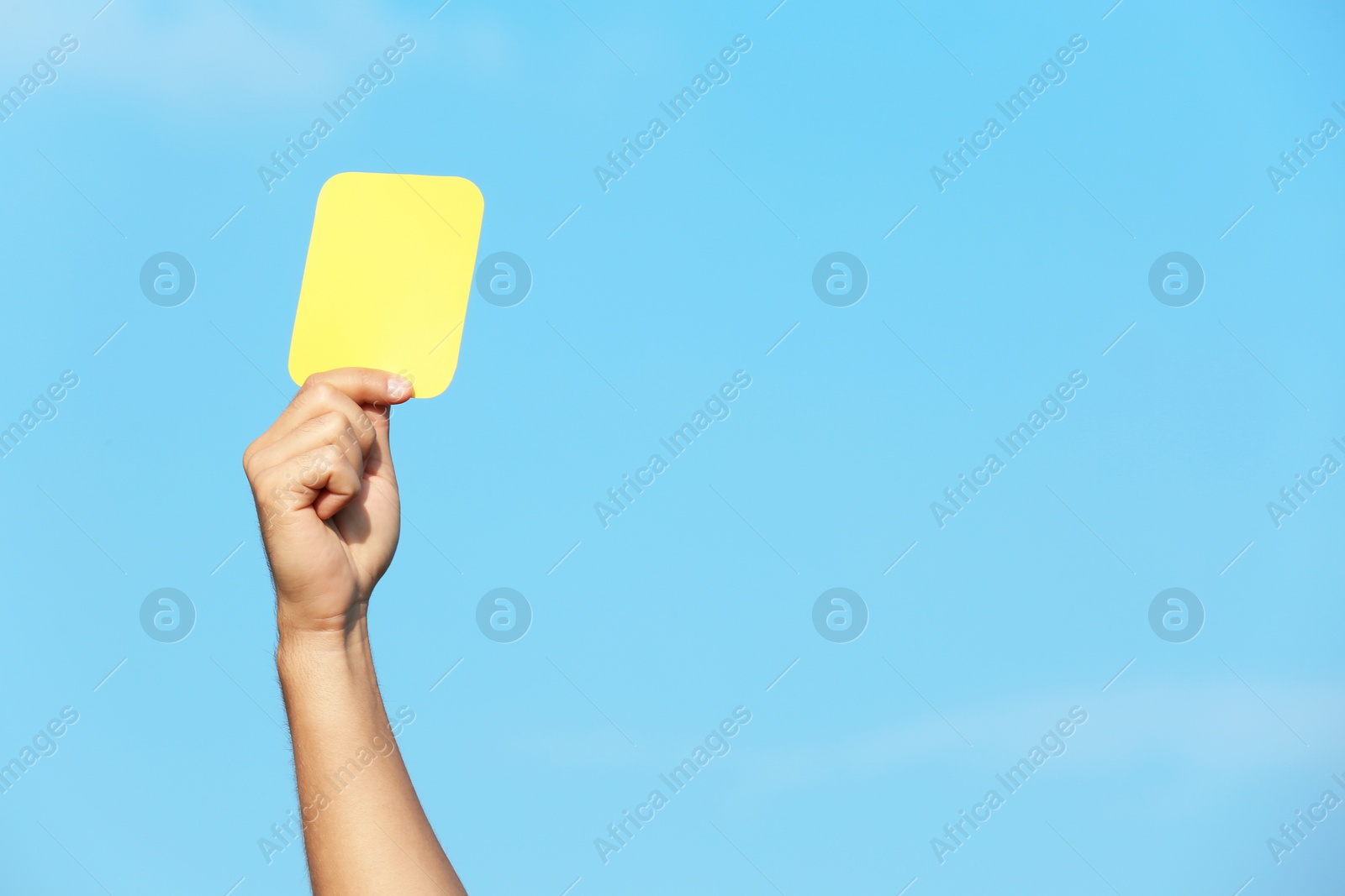 Photo of Football referee showing yellow card against blue sky, closeup with space for text
