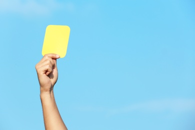 Football referee showing yellow card against blue sky, closeup with space for text