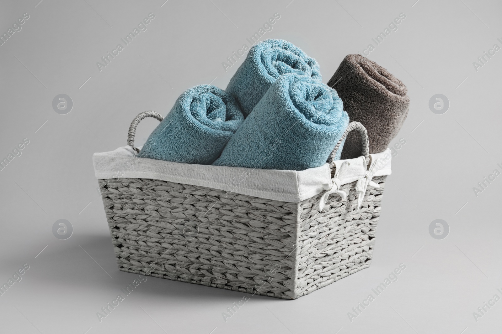 Photo of Basket with rolled towels on light background