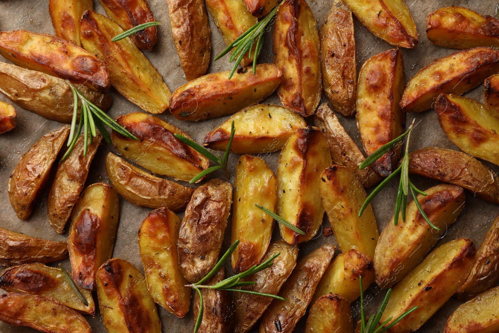 Photo of Tasty baked potato and aromatic rosemary on parchment paper, flat lay