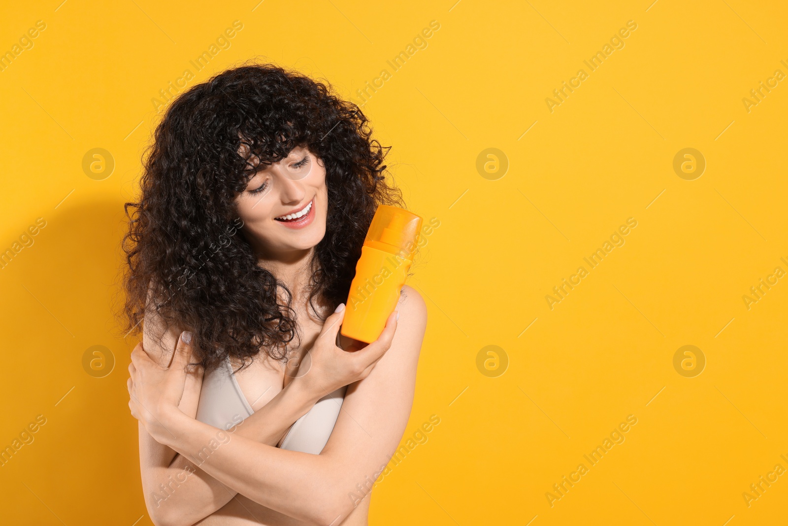 Photo of Beautiful young woman holding bottle of sun protection cream on orange background, space for text