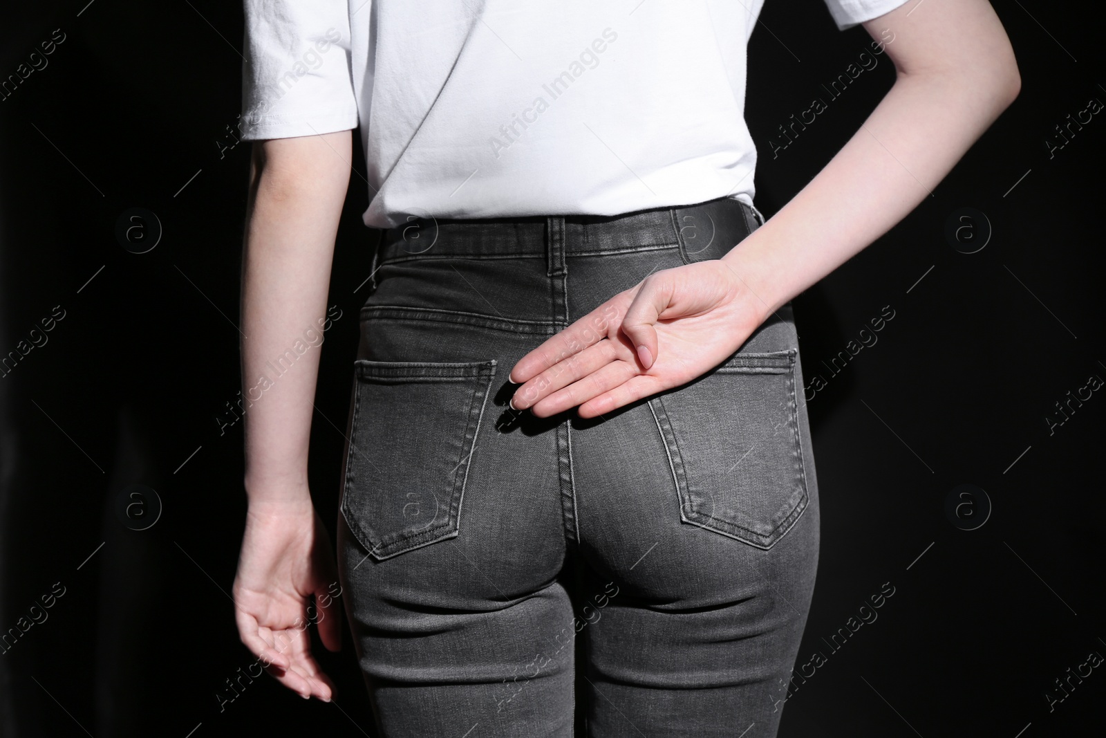 Photo of Woman showing open palm behind her back on black background, back view