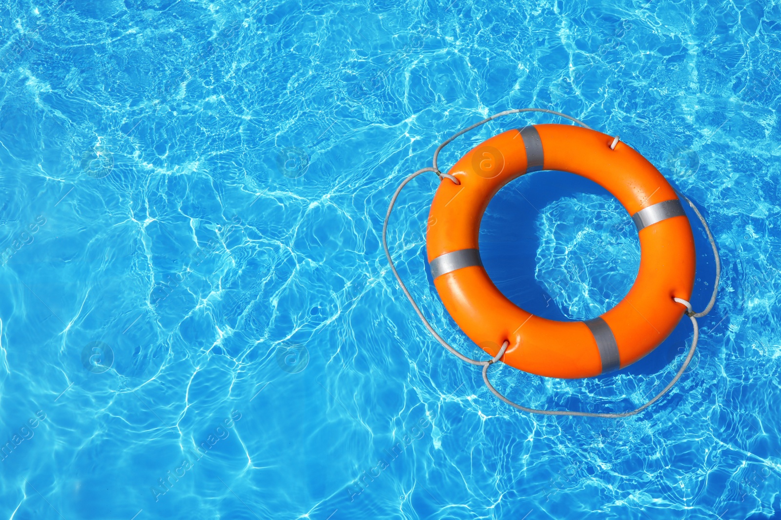 Photo of Lifebuoy floating in swimming pool on sunny day, top view with space for text