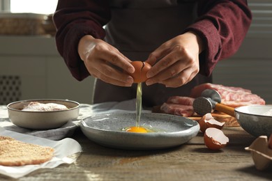 Photo of Woman cooking schnitzel at wooden table indoors, closeup