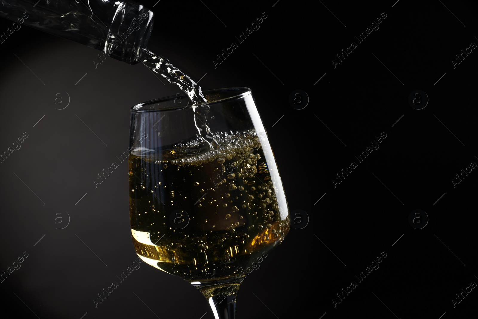 Photo of Pouring tasty aromatic wine in glass on dark background, closeup