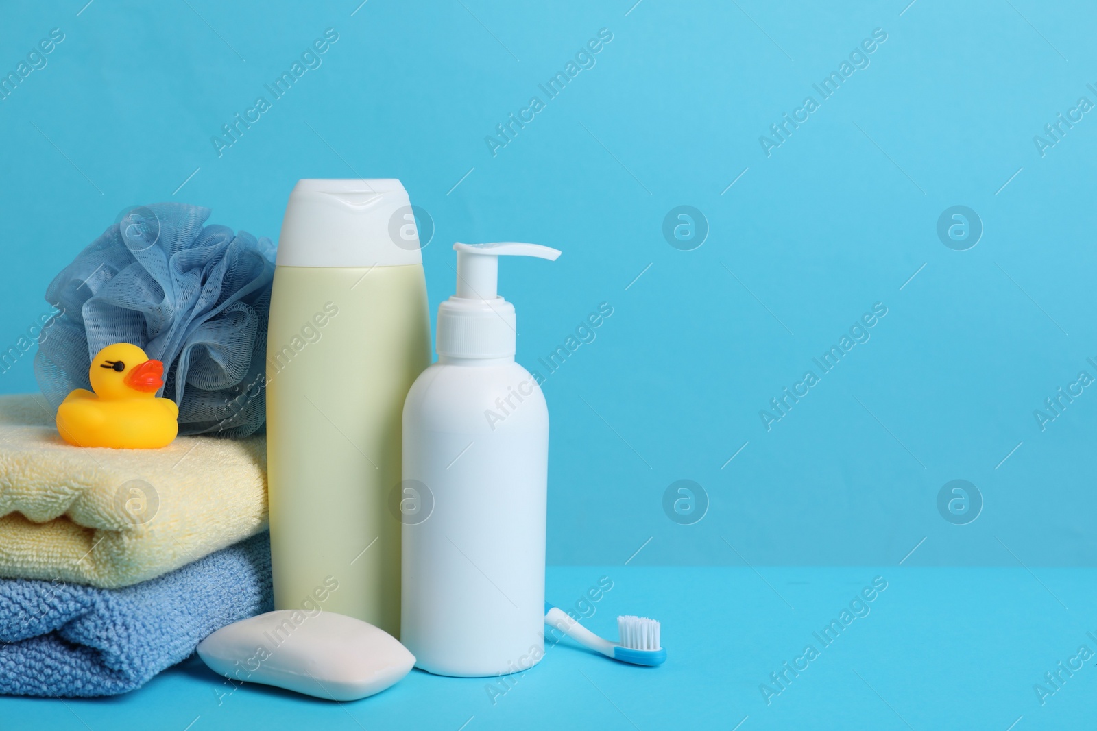 Photo of Baby cosmetic products, bath duck, accessories and towels on light blue background. Space for text