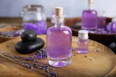 Photo of Natural herbal oil and lavender flowers on wooden plate against blurred background, closeup