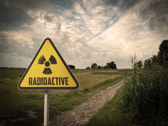Image of Radioactive pollution. Yellow warning sign with hazard symbol near contaminated area outdoors. Space for text