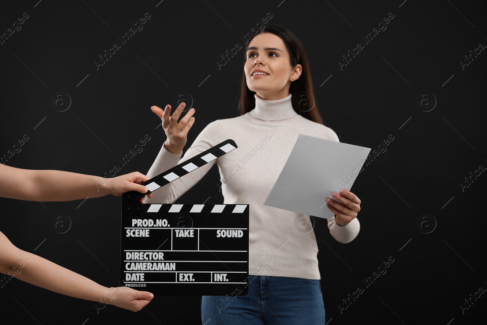 Photo of Actress performing while second assistant camera holding clapperboard on black background. Film industry