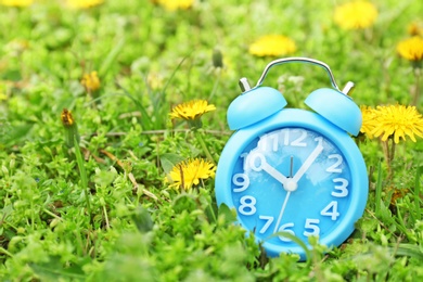 Alarm clock on green grass, outdoors. Time change concept