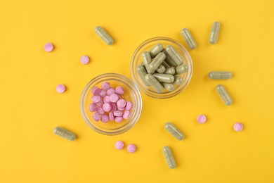 Different vitamin pills in glass bowls on yellow background, flat lay