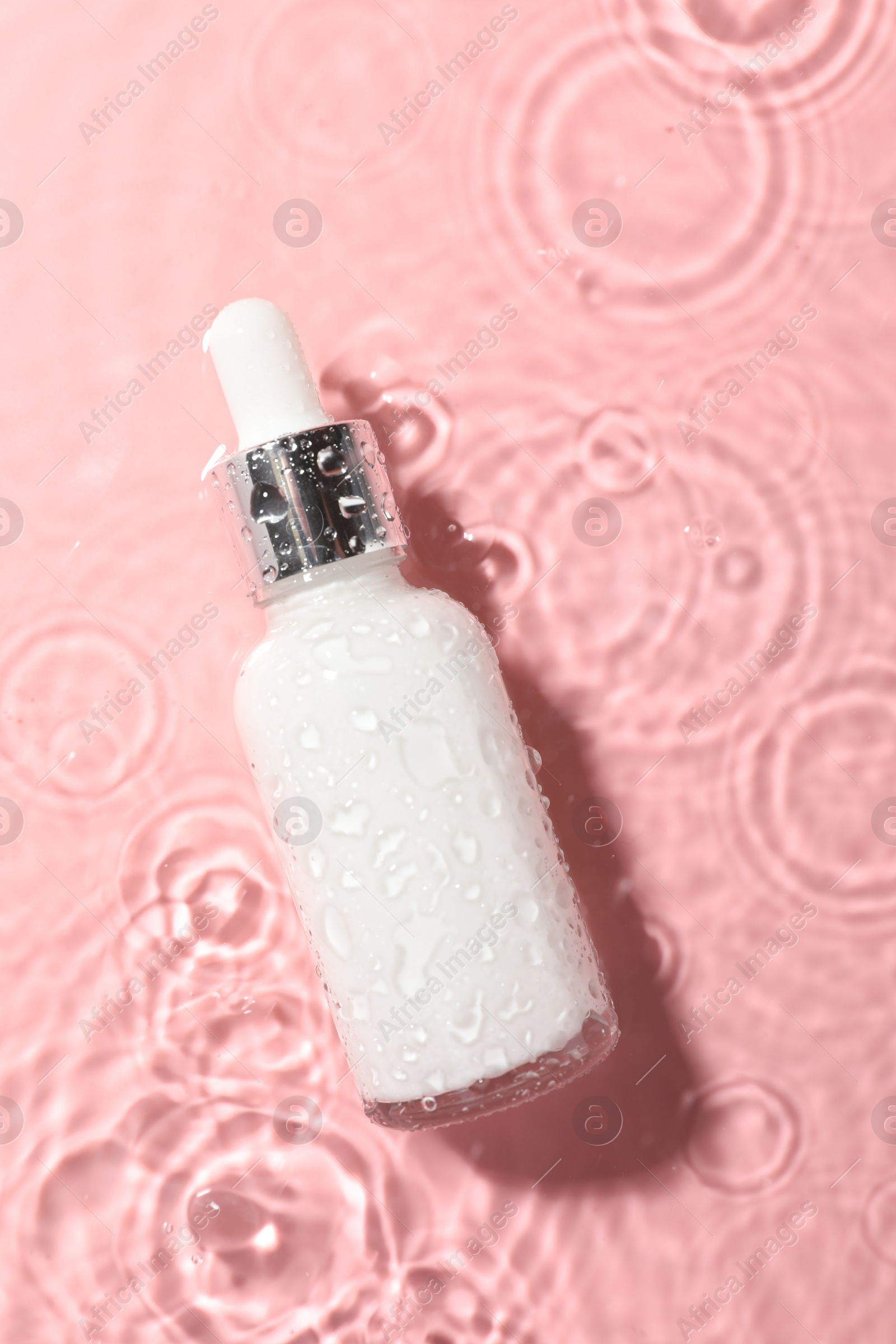 Photo of Bottle of cosmetic product in water on pink background, top view