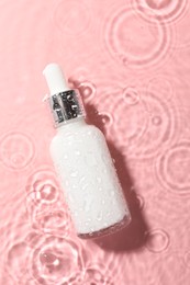 Photo of Bottle of cosmetic product in water on pink background, top view