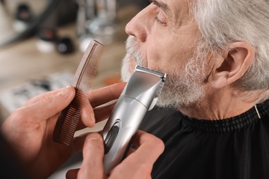 Photo of Professional barber trimming client's beard in barbershop, closeup