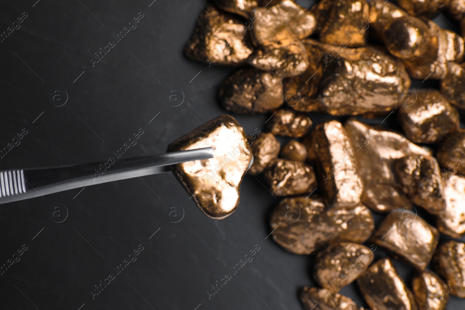 Photo of Tweezers with gold nugget above pile on black table, top view