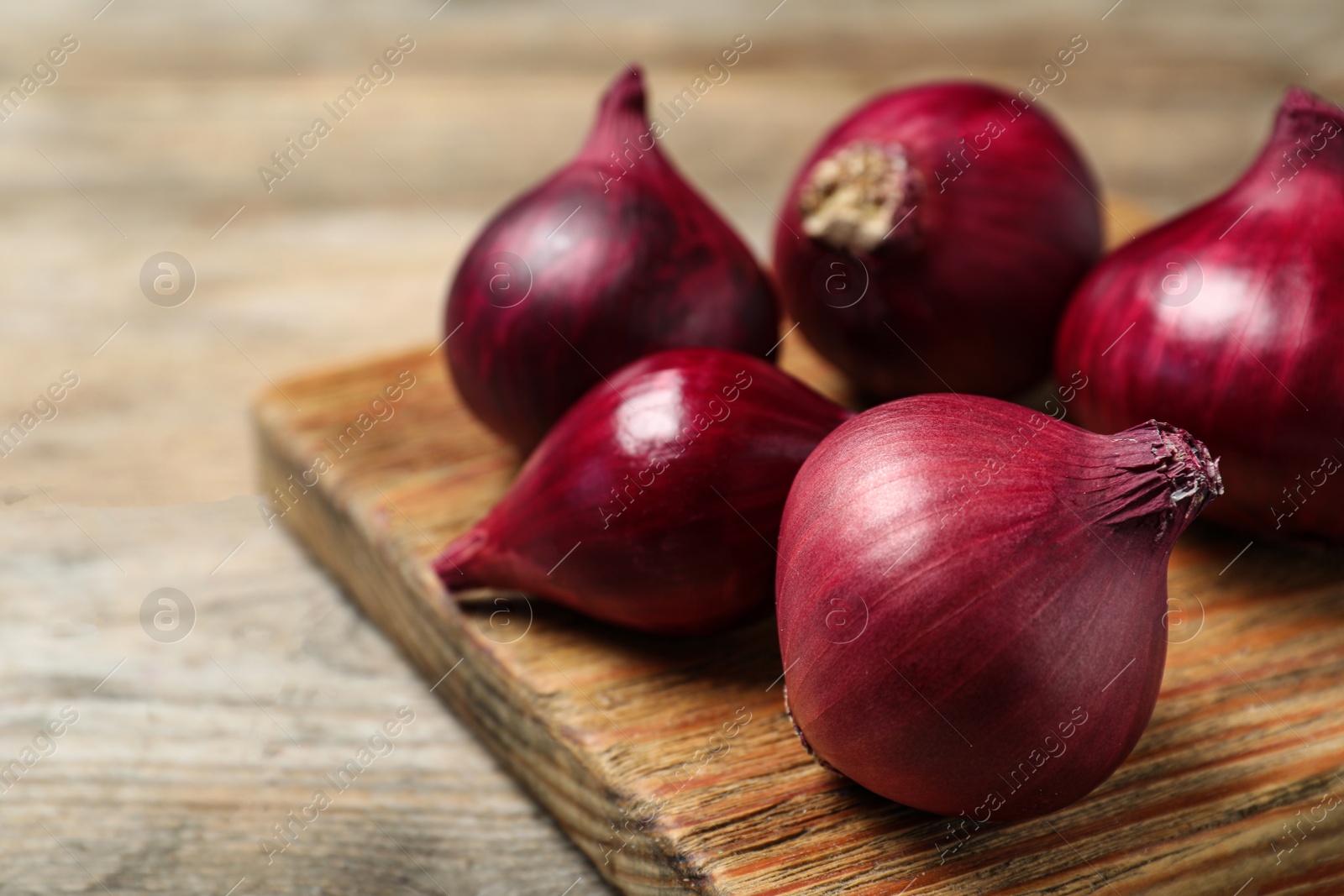 Photo of Board with ripe red onions on wooden table. Space for text