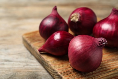 Board with ripe red onions on wooden table. Space for text