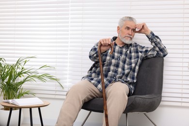 Photo of Senior man with walking cane sitting on armchair at home
