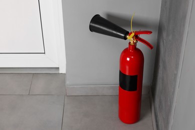 Red fire extinguisher near grey wall, space for text