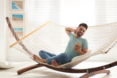 Young man using smartphone in hammock at home