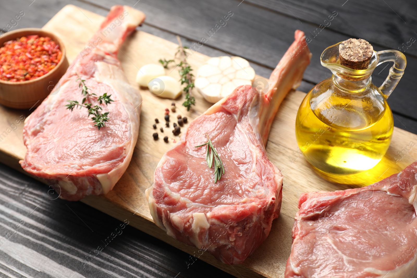 Photo of Fresh tomahawk beef cuts, spices and oil on black wooden table, closeup