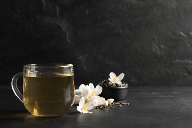 Photo of Glass cup of jasmine tea and fresh flowers on black table. Space for text