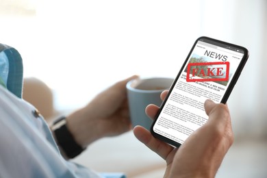 Image of Fake information. Man using mobile phone to read news at home, closeup