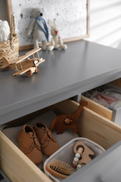 Photo of Open cabinet drawer with baby shoes and accessories in child room