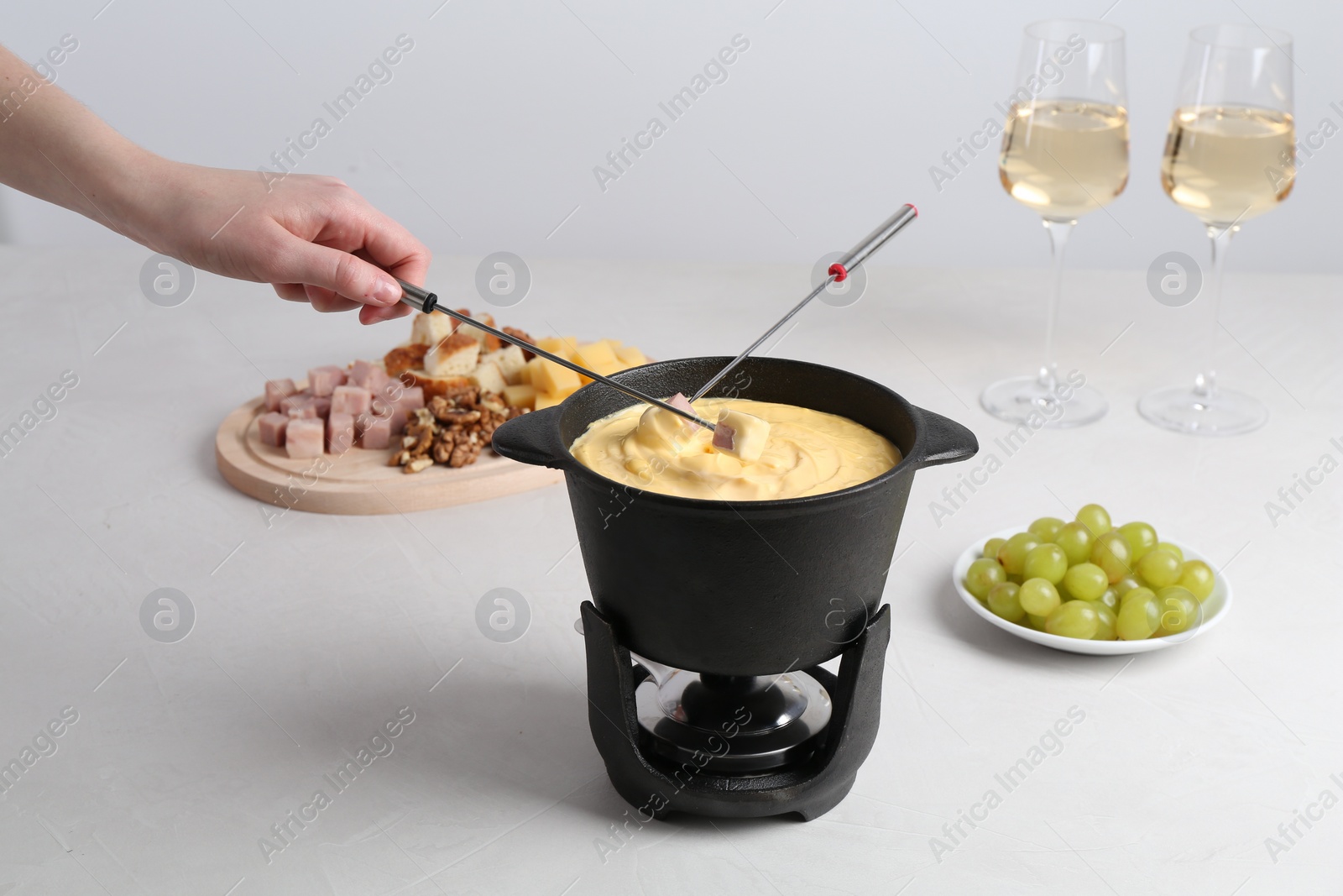 Photo of Woman dipping ham into fondue pot with tasty melted cheese at white table, closeup