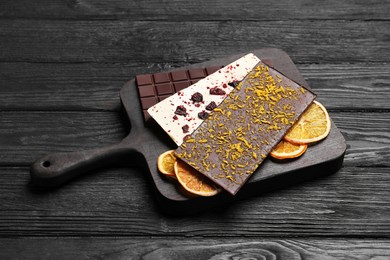 Board and different chocolate bars with freeze dried fruits on black wooden table