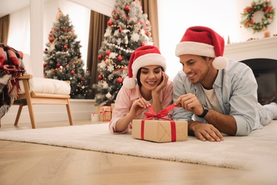 Photo of Happy couple in Santa hats with Christmas gift at home