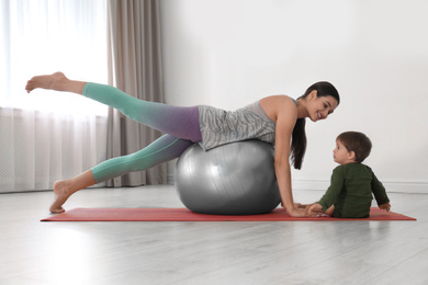 Photo of Young woman doing exercise with her son indoors. Home fitness