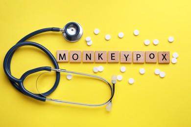 Word Monkeypox made of wooden cubes, pills and stethoscope on yellow background, flat lay