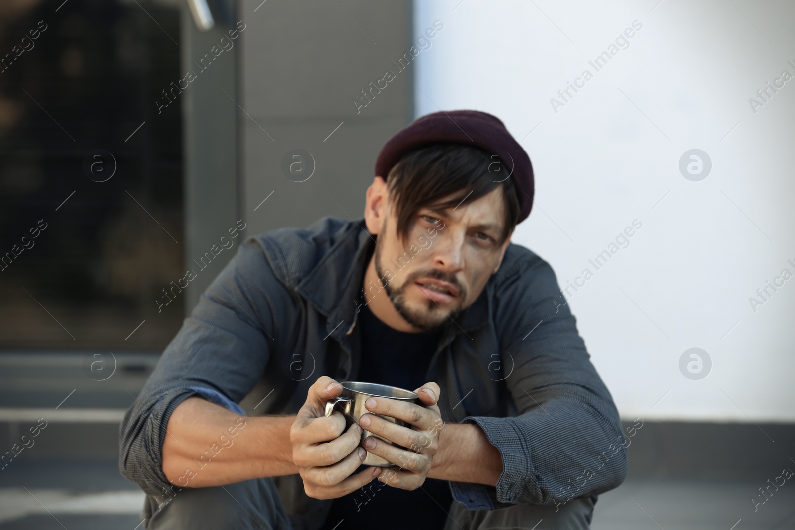 Photo of Poor man with mug begging on city street