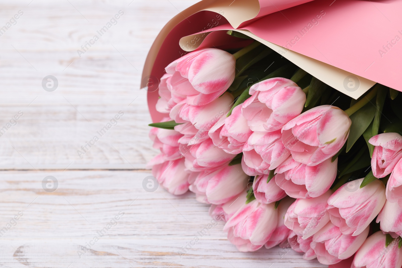 Photo of Beautiful bouquet of fresh pink tulips on white wooden table, closeup. Space for text
