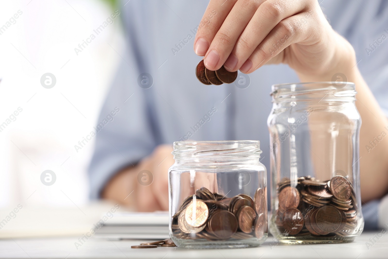 Photo of Woman putting money into glass jar at table, closeup