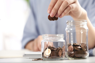 Woman putting money into glass jar at table, closeup