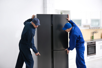 Professional workers carrying modern refrigerator in kitchen